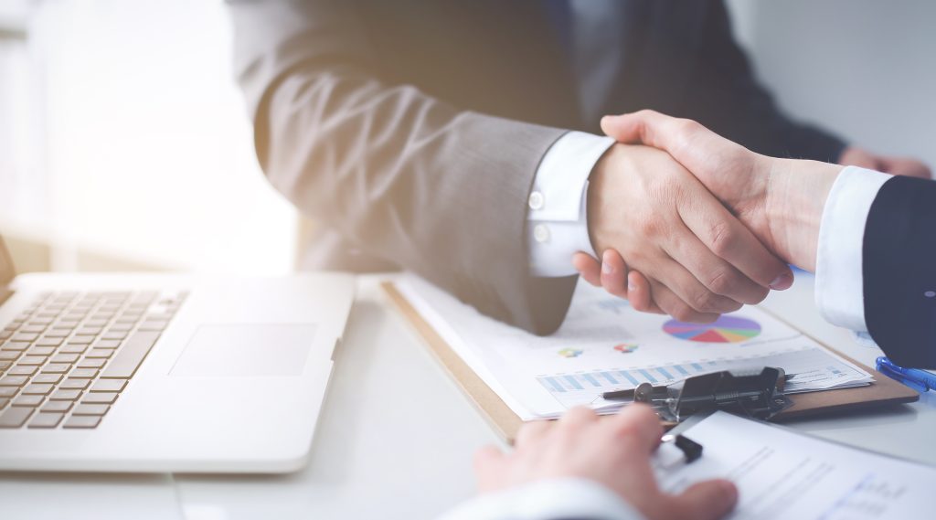 Two professionals shaking hands over documents and a laptop, representing auto dealership coupon savings, special offers, and financing deals.