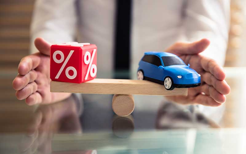 A blue toy car and red percent sign cube on wood held by a person