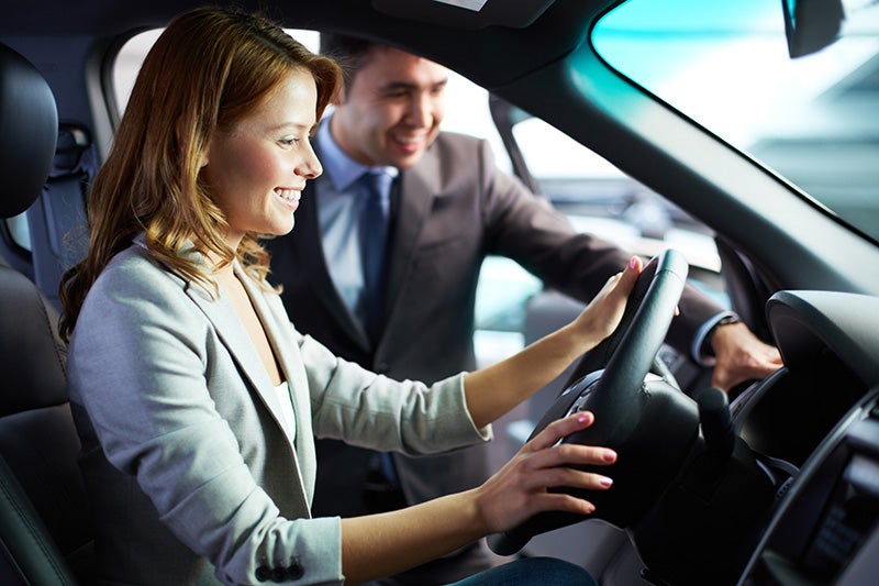 A woman seated in the driving seat while a salesperson talks with her